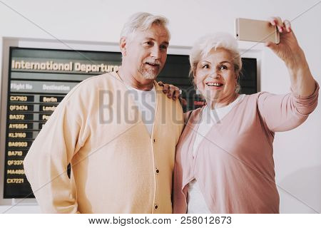 Old Couple Taking Photo In Airport In Waiting Room. Senior Person In Airport. Tourism Concept. Coupl