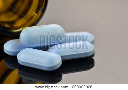 Blue Caplets And Amber Bottle With Reflection On Dark Background.
