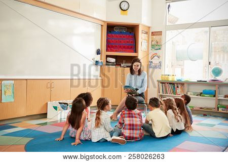 School kids sitting on the floor gathered around teacher