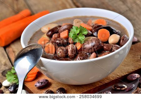 Detail Of Bowl Of Bean Soup With Large Beans , Spoon, Carrots, Parsley And Marjoram