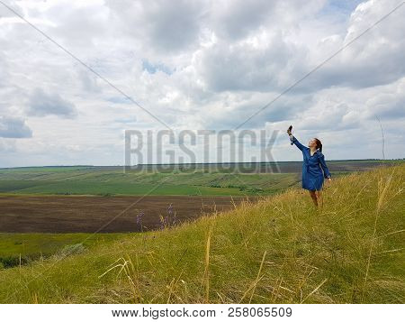 A Young Woman With Red Hair And A Blue Denim Dress Is In The Mountains Outside The City And Is Tryin