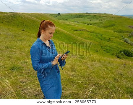 A Young Woman With Red Hair And A Blue Denim Dress Is In The Mountains Outside The City And Is Tryin