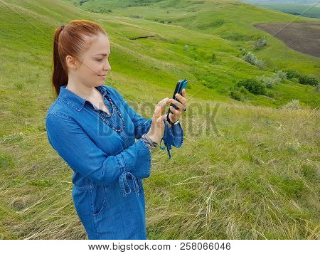 A Young Woman With Red Hair And A Blue Denim Dress Is In The Mountains Outside The City And Is Tryin
