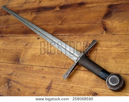 Old Medieval Sword On A Wooden Table. Ancient Armoury, Knightly Weapon Of The Middle Ages