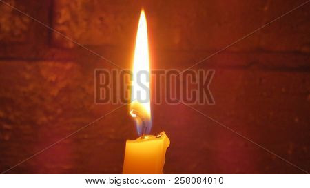 Wax Chirch Candle Burning In Front Of Red Brick Wall
