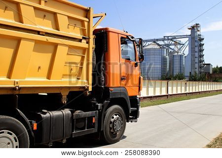 Orange Truck On The Territory Of Grain Storage In Sunny Weather Harvesting