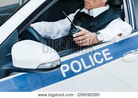 Partial View Of Male Police Officer In Bulletproof Vest Holding Walkie-talkie In Car