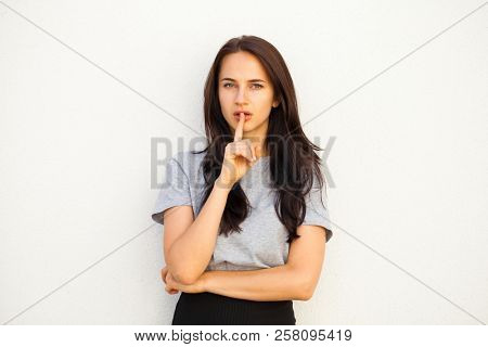 Woman requires silence. Young beautiful brunette girl has put forefinger to lips as sign of silence, isolated on white background