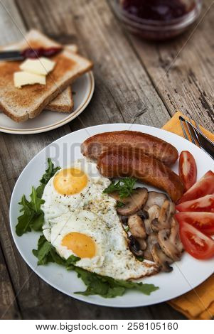 English Breakfast. Eggs, Sausages, Mushrooms, Tomatoes, Toast Bread. Eating Tasy Food Over Rustic Wo