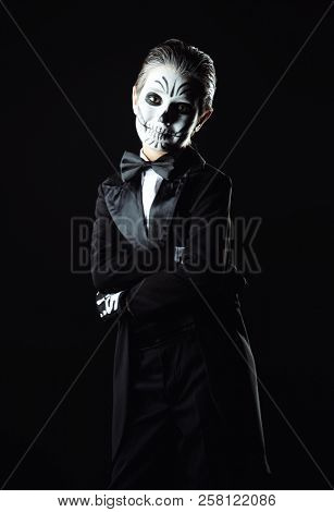 Portrait of a child boy with carnival make-up of a skeleton wearing elegant tail-coat. Studio shot over black background. Halloween. Dia de los muertos. The Day of the Dead.