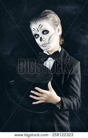 Portrait of a child boy with carnival make-up of a skeleton wearing elegant tail-coat. Studio shot over black background. Halloween. Dia de los muertos. The Day of the Dead.