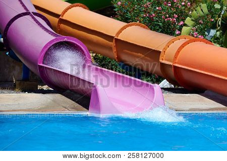 Colorful Plastic Water Slides In Waterpark. There Are Splashes Left By Person Sliding Down.