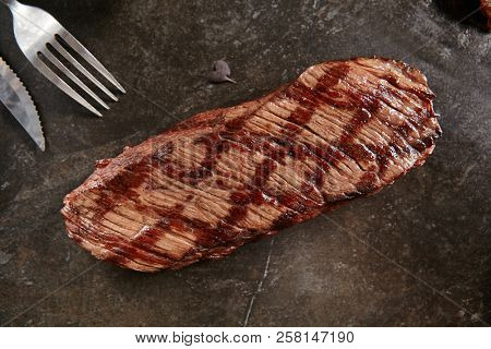 Hot Grilled Whole Denver Steak on Black Stone Background. Fresh Juicy Medium Rare Beef Grillsteak. Barbecue Meat Top View Close Up