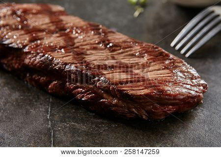 Hot Grilled Whole Denver Steak on Black Stone Background. Fresh Juicy Medium Rare Beef Grillsteak. Barbecue Meat Close Up