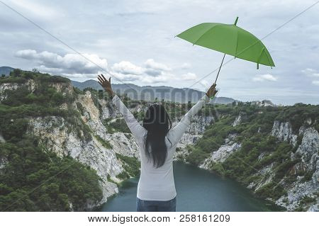 Hipster Young Girl With Green Umbella Enjoying Sunset On Peak Mountain. Tourist Traveler On Backgrou