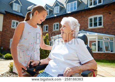 Granddaughter Visiting Grandmother Sitting In Motorized Wheelchair In Retirement Home