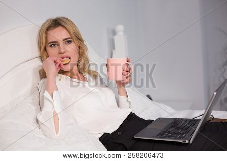 Nice Businesswoman Having Coffee And Buscuits In Bed. Relaxing While Working.