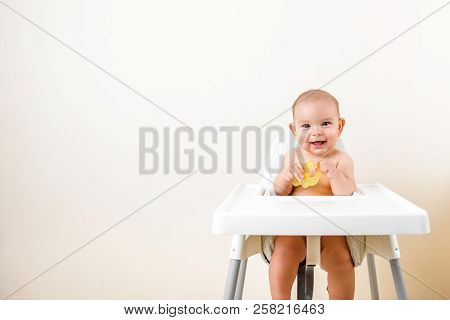 Cute Baby Infant Kid Biting Sitting In Highchair And Chewing Yellow Eething Toy Copy Space Bright Mi