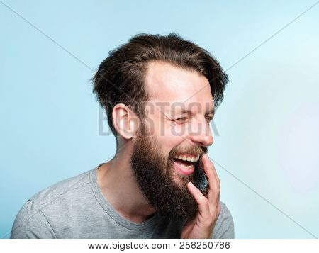 Happiness Enjoyment And Laugh. Man With A Wide Grin. Portrait Of A Young Bearded Guy On Blue Backgro
