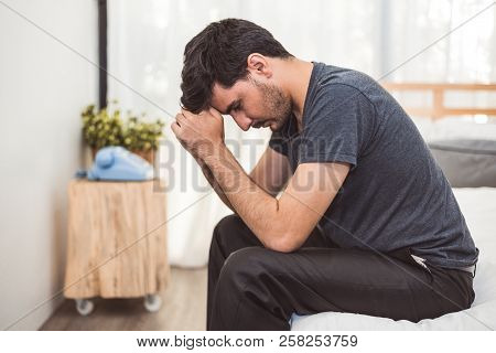 Worried Man Sitting On Bed With Hand On Forehead In Bedroom In Serious Mood Emotion. Major Depressiv