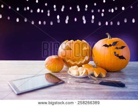 holidays, halloween and technology concept - jack-o-lantern or carved pumpkin with tablet pc computer and knife on wooden table over ultra violet background