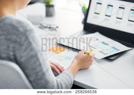 app design, technology and business concept - web designer or developer with sketches and laptop computer working on user interface at office