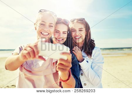 summer vacation, holidays, travel, technology and people concept- group of smiling young women taking sulfide with smartphone on beach
