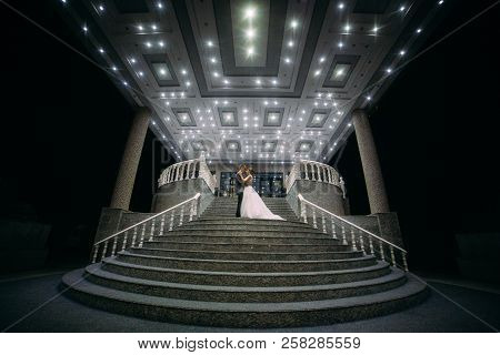The Bride And Groom Stand On The Beautiful Porch Of The Hotel At Night