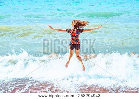 A Young Girl In Shorts Stands With Her Back Against The Background Of Big Waves