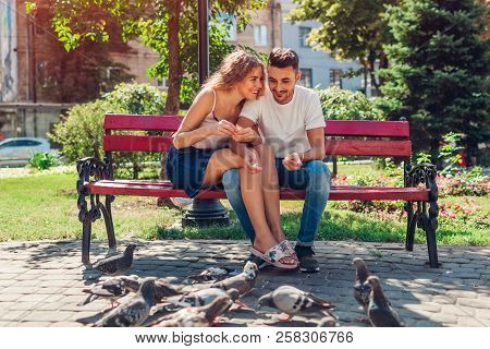 Young Mixed Race Couple In Love Feeding Bidrs In Summer Park. Man And Woman Thowing Bread To Doves