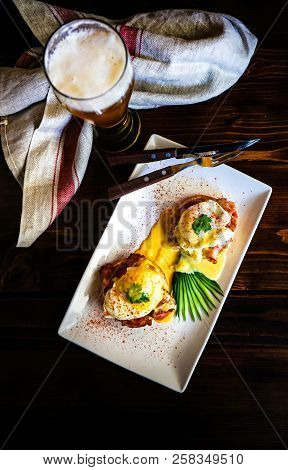 Rustic Lunch Set With Benedict Eggs And Cucumber Salad On Dark Wooden Table