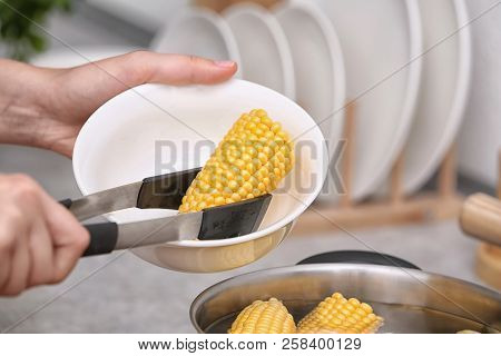 Woman Putting Raw Corn Cob Into Stewpot, Closeup