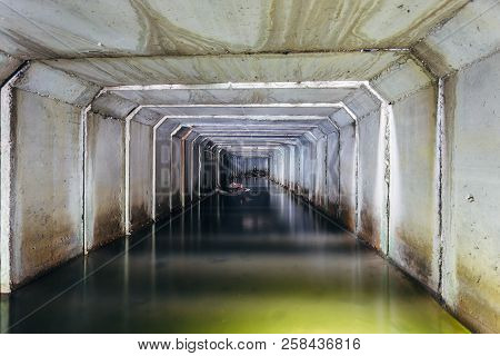 Flooded Sewer Tunnel Is Reflecting In Water. Dirty Urban Sewage Flowing Throw Rectangular Sewer Tunn