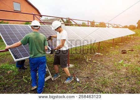 Team Of Workers Finish Assembling Exterior Stand-alone Solar Photo Voltaic Panel System In Green Fie