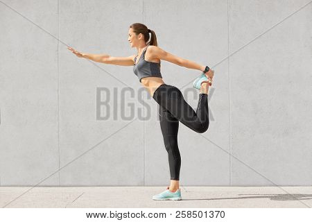 Photo Of Slim Fitness Woman Raises Leg, Stands In Special Pose, Tries To Cure Osteochondrosis, Has S
