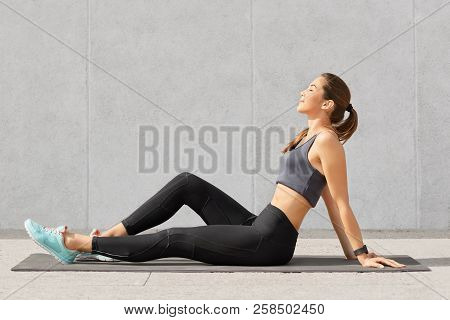 People, Sport And Relaxation Concept. Relaxed Fitness Woman With Perfect Figure Sits On Exercise Mat
