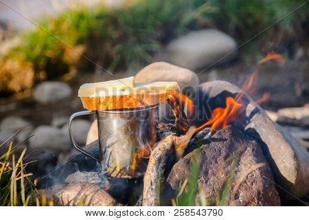 Warming cup of tea with cheese butterbrot (sandwich) on burning campfire at wild camping