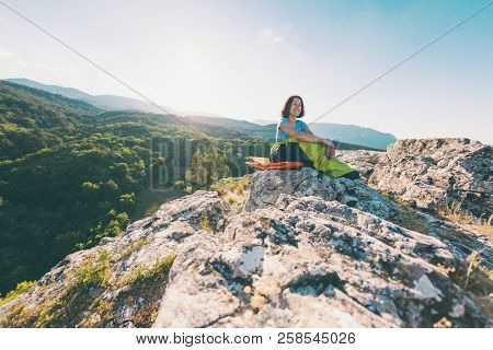 A Woman Is Sitting In A Sleeping Bag On Top Of A Mountain. A Smiling Girl Rests After A Climb. The B