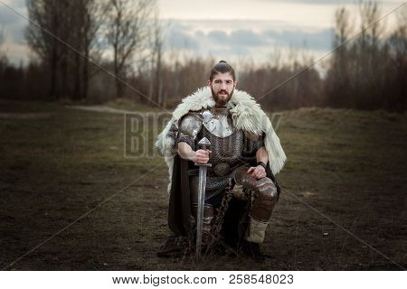 Knight In Armor With A Sword In Hand, Standing On One Knee.