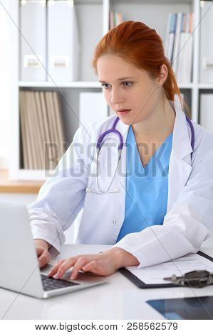 Brunette Female Doctor Using Laptop Computer In Hospital. Healthcare, Insurance And Medicine Concept