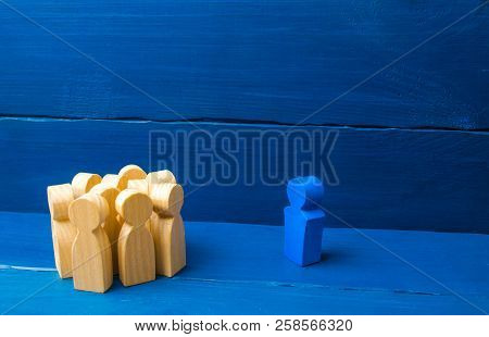 The Crowd Of Wooden Figures Of People Stand Distantly And Look At The Blue Man. The Person Tries To 