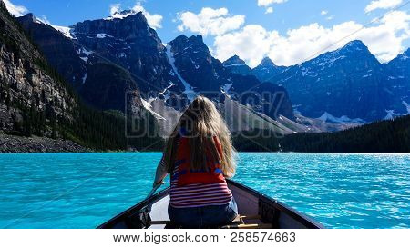 Girl Paddling Through Bright Blue Lake In The Mountains