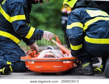 Firefighters Putting An Injured Woman Into A Plastic Stretcher After A Car Accident.