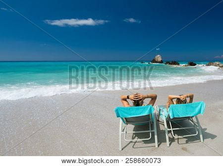 Couple on sunbeds relaxing at the beach in Lefkada Greece