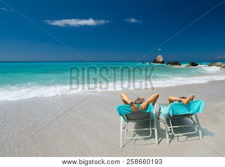 Couple on sunbeds relaxing at the beach in Lefkada Greece