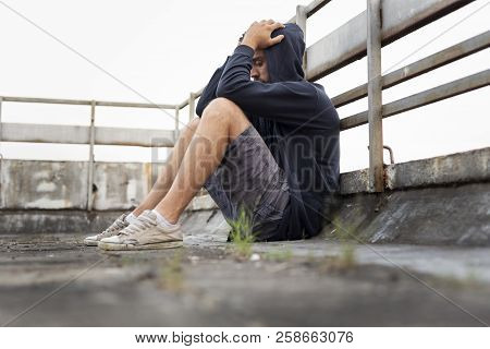 Depressed, Desperate Young Man Sitting On The Building Rooftop Terrace, Wearing Hoodie, Holding Head