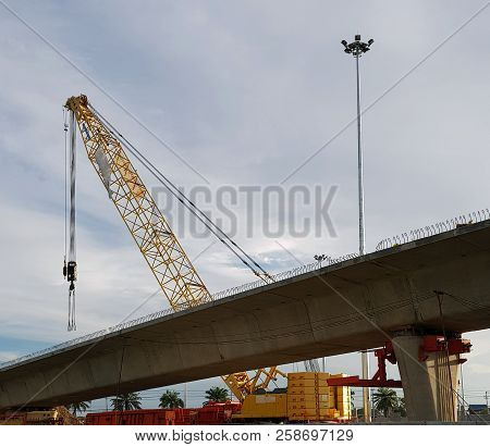 Construction Crane Being Assembled Using Car Crane. Silhouette Of A Worker Reaching For A Crain Cab 