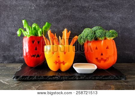 Healthy Halloween Food. Vegetables And Dip In Jack O Lantern Bell Peppers. Side View Against A Dark 