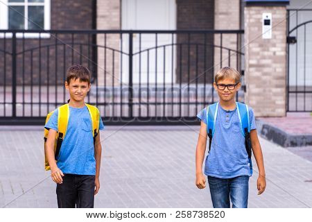 Two Happy Shoolboys With Backpacks Go To School In The Morning.