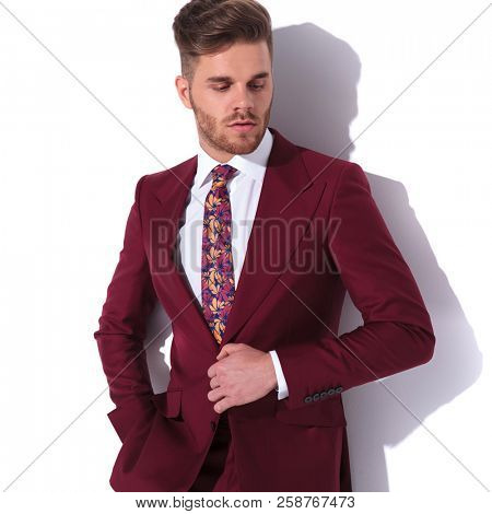 young sexy elegant man unbuttoning his suit and looks down on white background